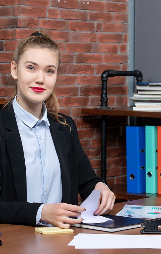 Top view of young female office worker sitting at her desk and posing for camera