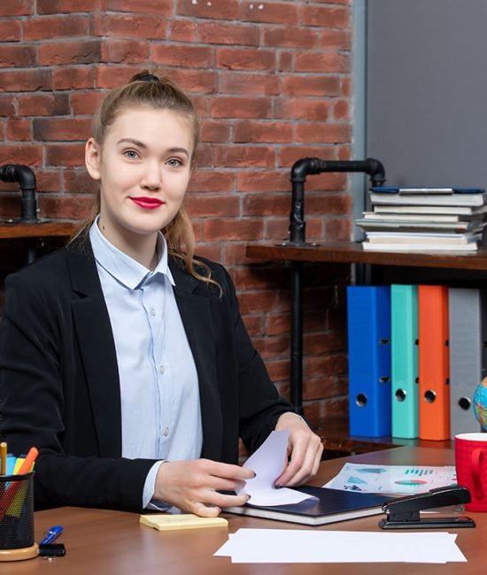 Top view of young female office worker sitting at her desk and posing for camera
